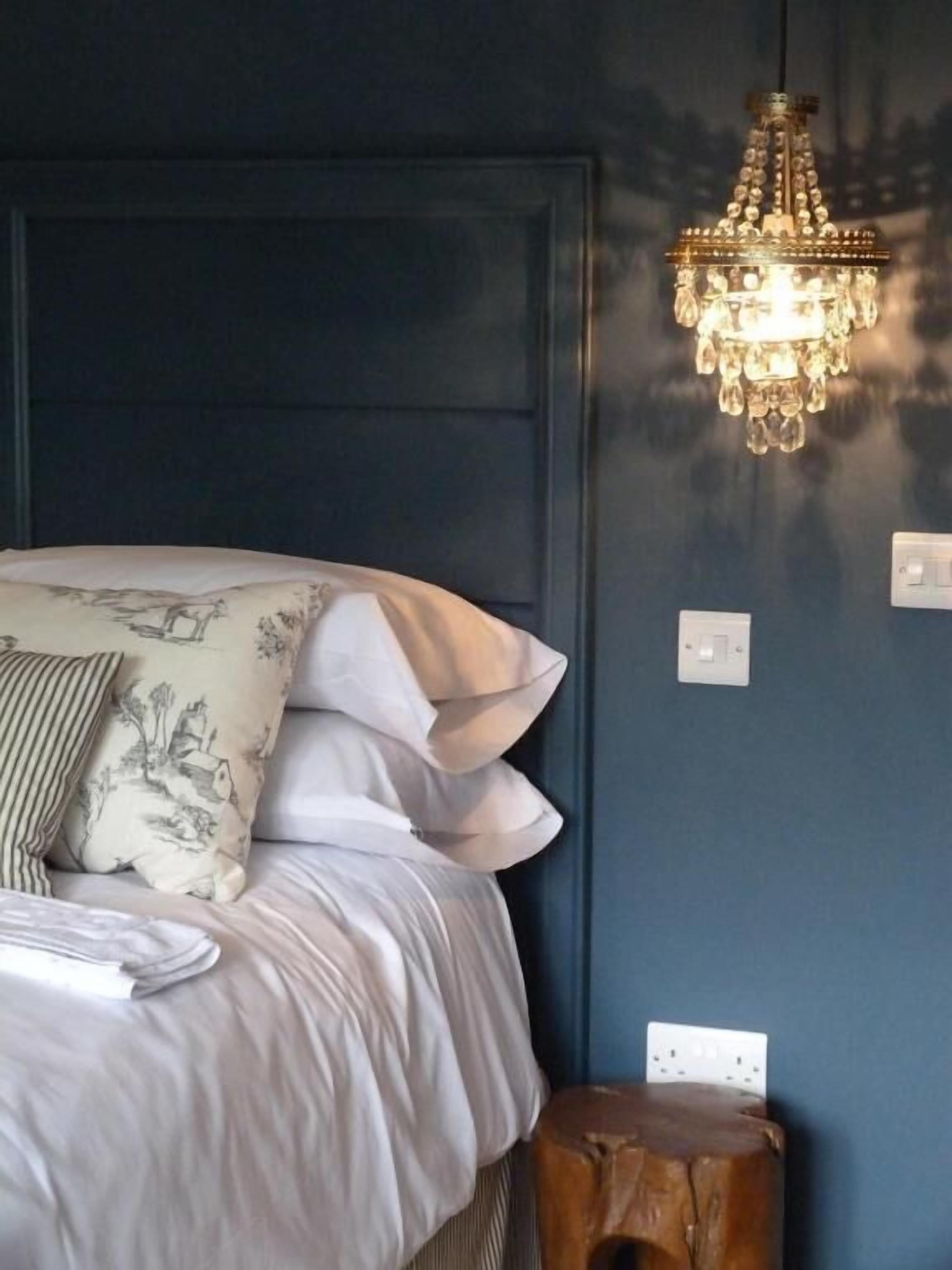 A bedroom with a bed, pillows, a wooden stool, and a chandelier.