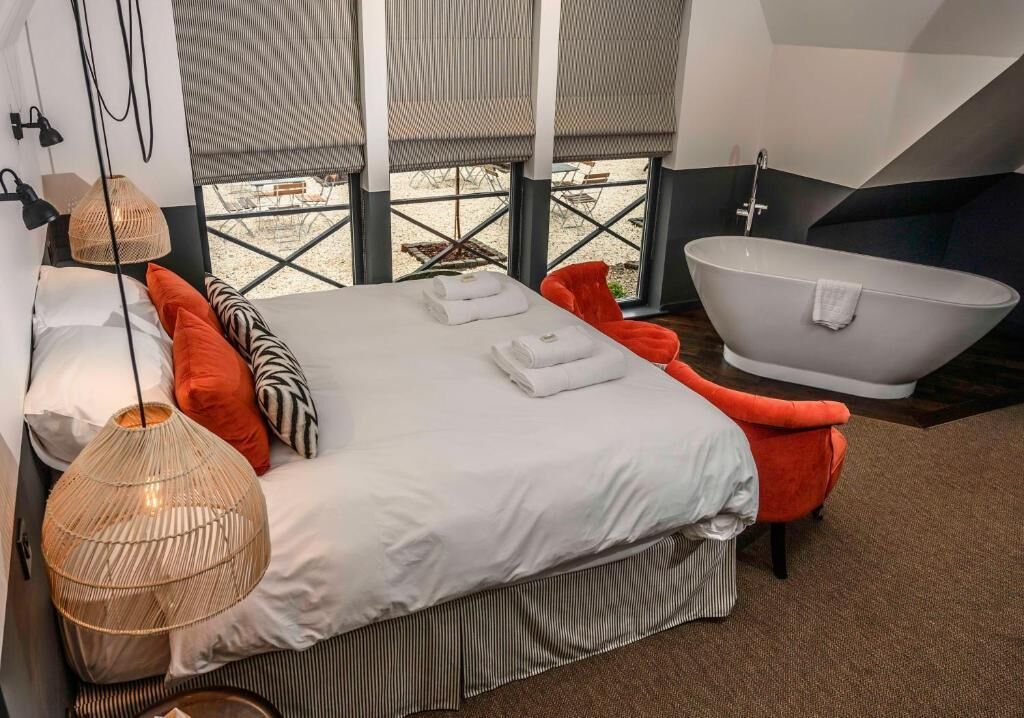 A modern bedroom with a large bed, a bathtub, and a view of the outdoors.