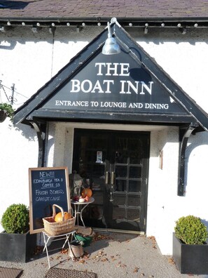 The exterior of The Boat Inn, featuring a signboard advertising new offerings like Edinburgh Tea & Coffee Co, fresh scones, and carrot cake.