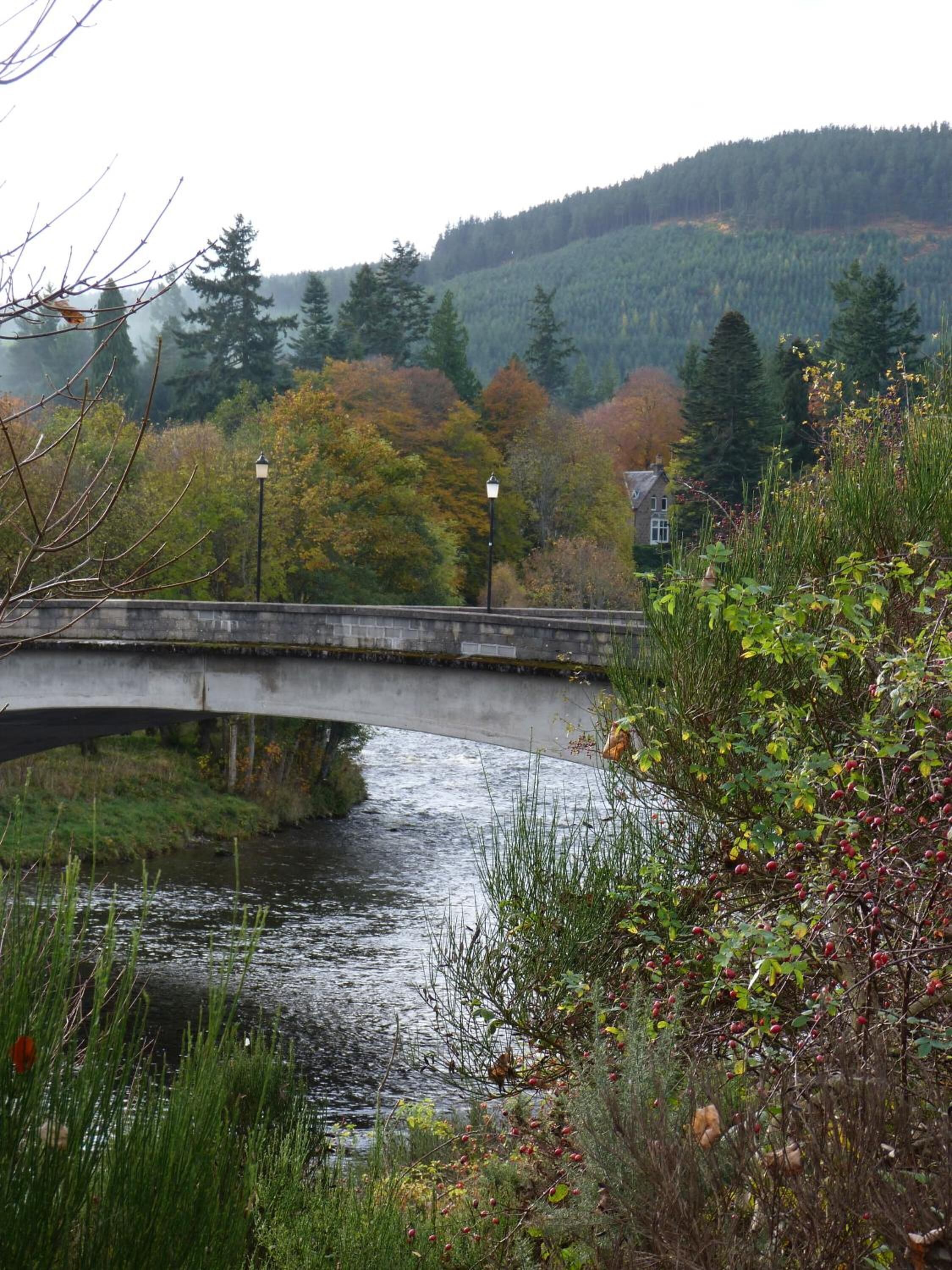 Un pont de pierre enjambant une rivière paisible, entouré d’un feuillage automnal et avec une colline boisée en arrière-plan.