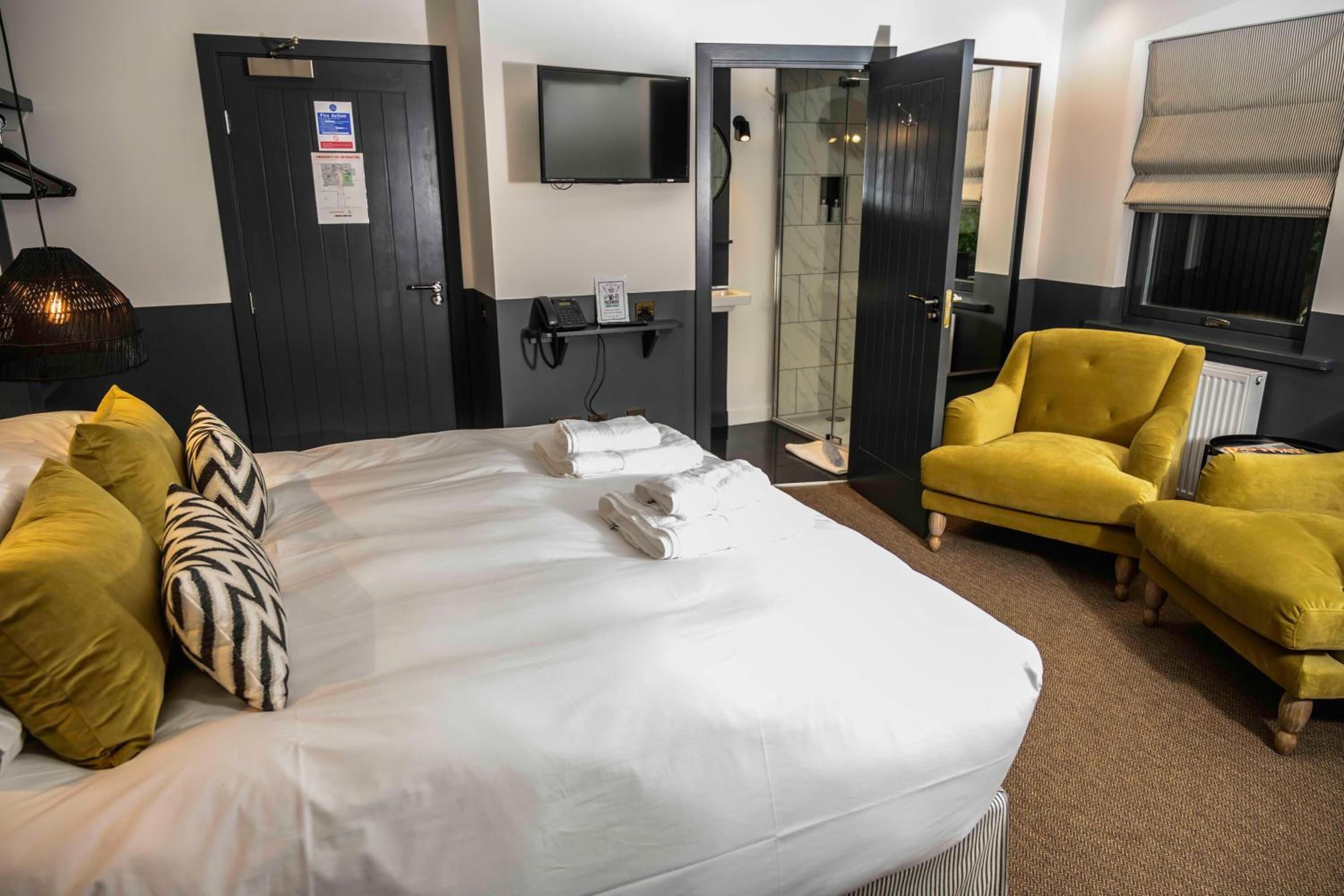Een hotelkamer met een bed, een televisie, een douche en een gele fauteuil.