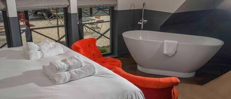Una habitación de hotel moderna con una cama grande, una silla roja y una bañera independiente.