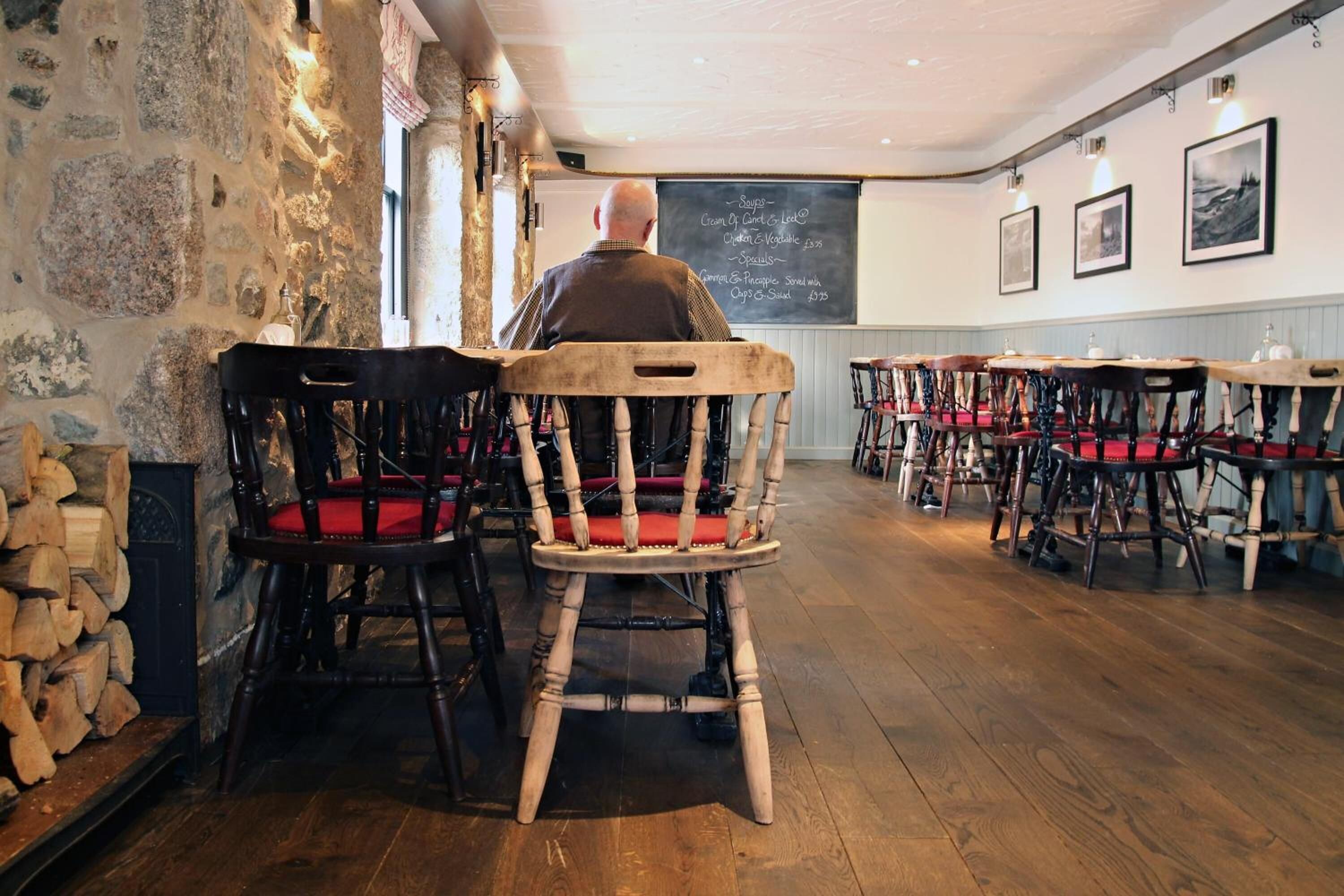 A rustic interior with wooden chairs and tables, stone walls, and a chalkboard menu.