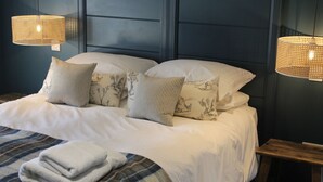 A neatly made bed with white linens and decorative pillows, a plaid blanket, and two woven wall lamps.
