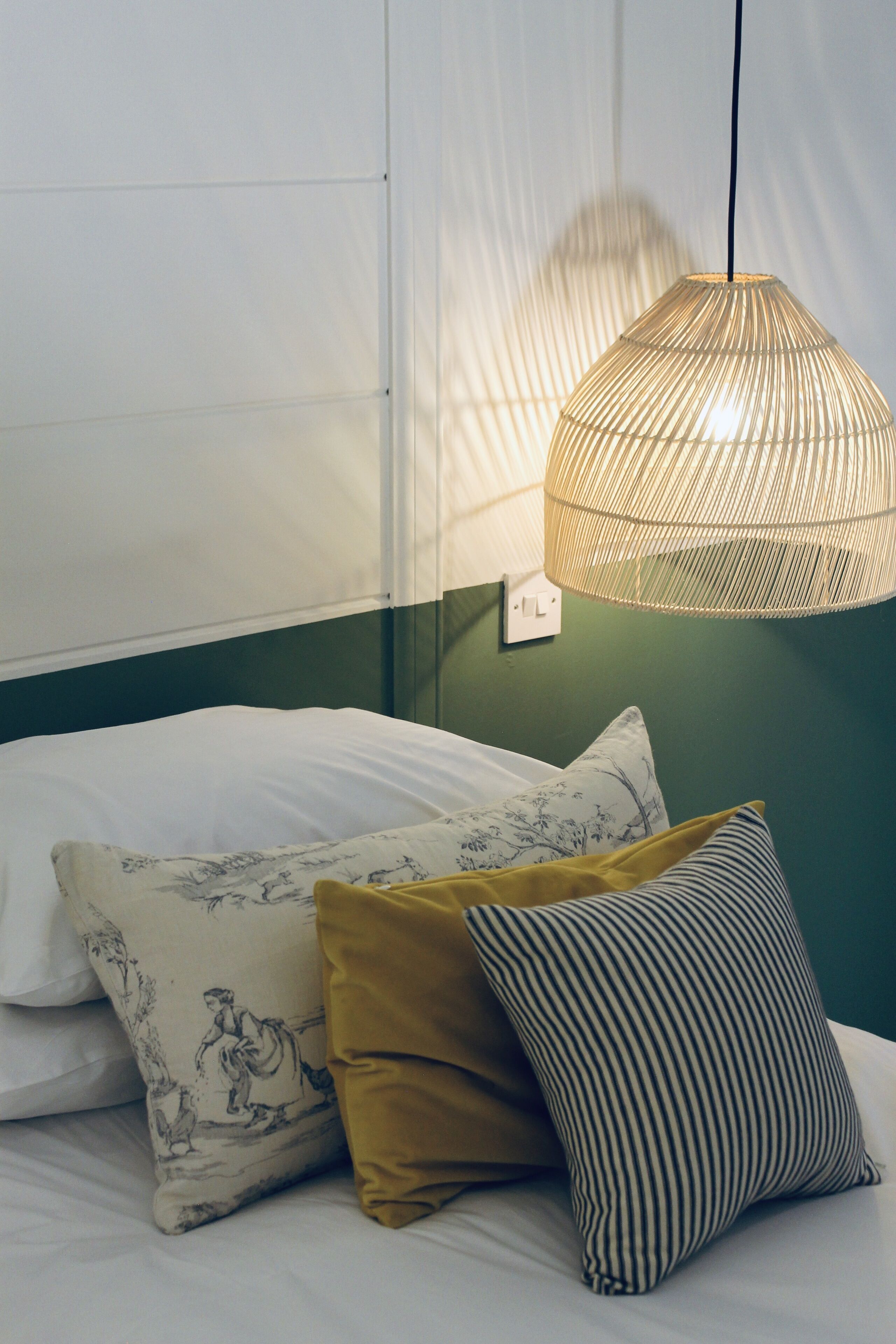 A bed with white and patterned pillows, a mustard-colored pillow, and a striped pillow.