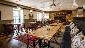 A restaurant with wooden tables and chairs, a stone wall, and a fireplace.