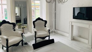 A modern living room with two upholstered chairs, a white fireplace, and a flat-screen TV mounted on the wall. - Apartamenty Campari (Torun)
