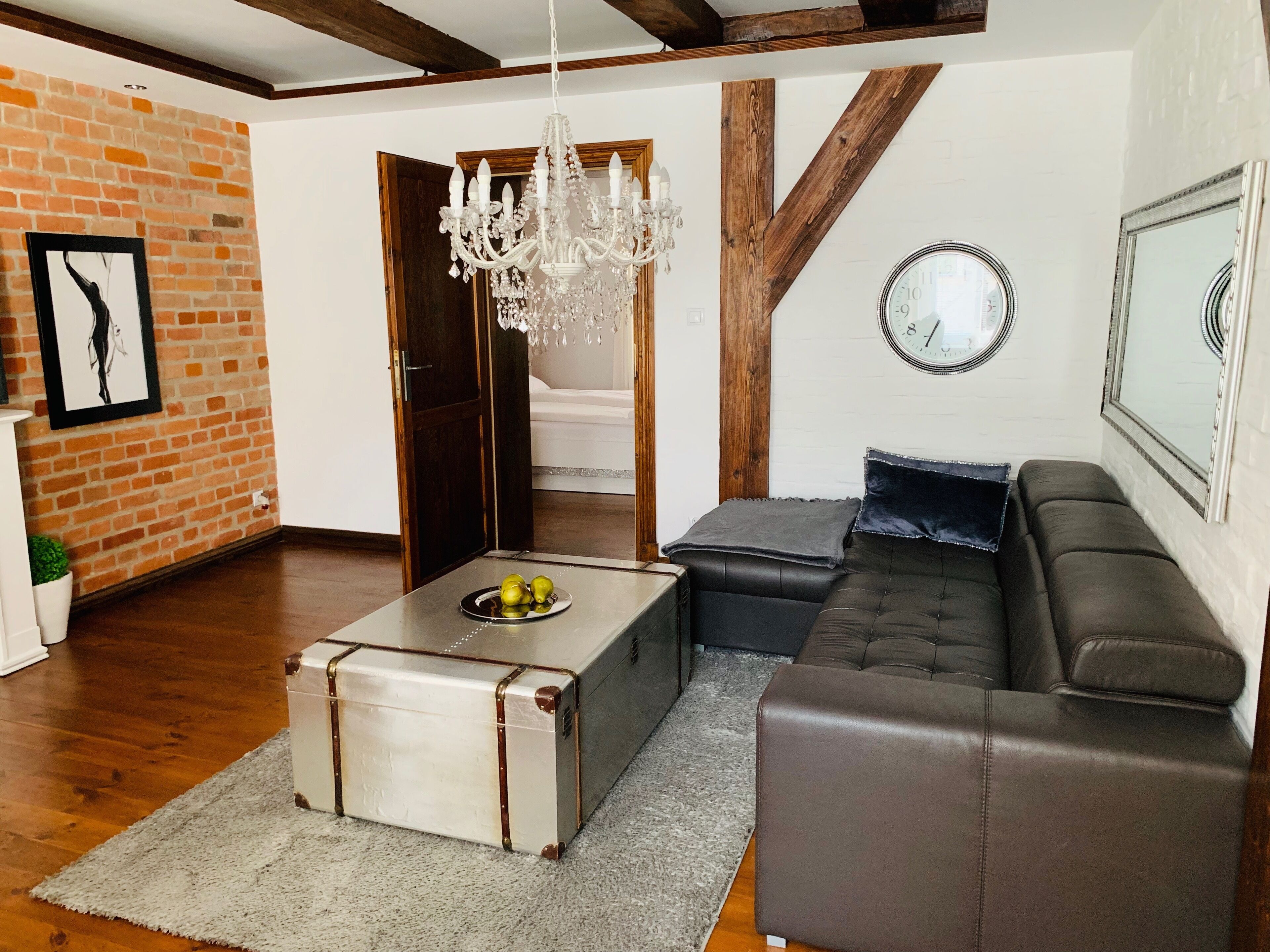 Ein Wohnzimmer mit einem Ledersofa, einem Couchtisch in Form eines alten Koffers, einer Chandelüster und einer Wanduhr.