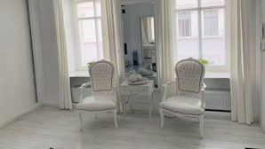 A room with two white upholstered chairs, a vanity with a mirror, and large windows with white curtains. - Apartamenty Campari (Torun)