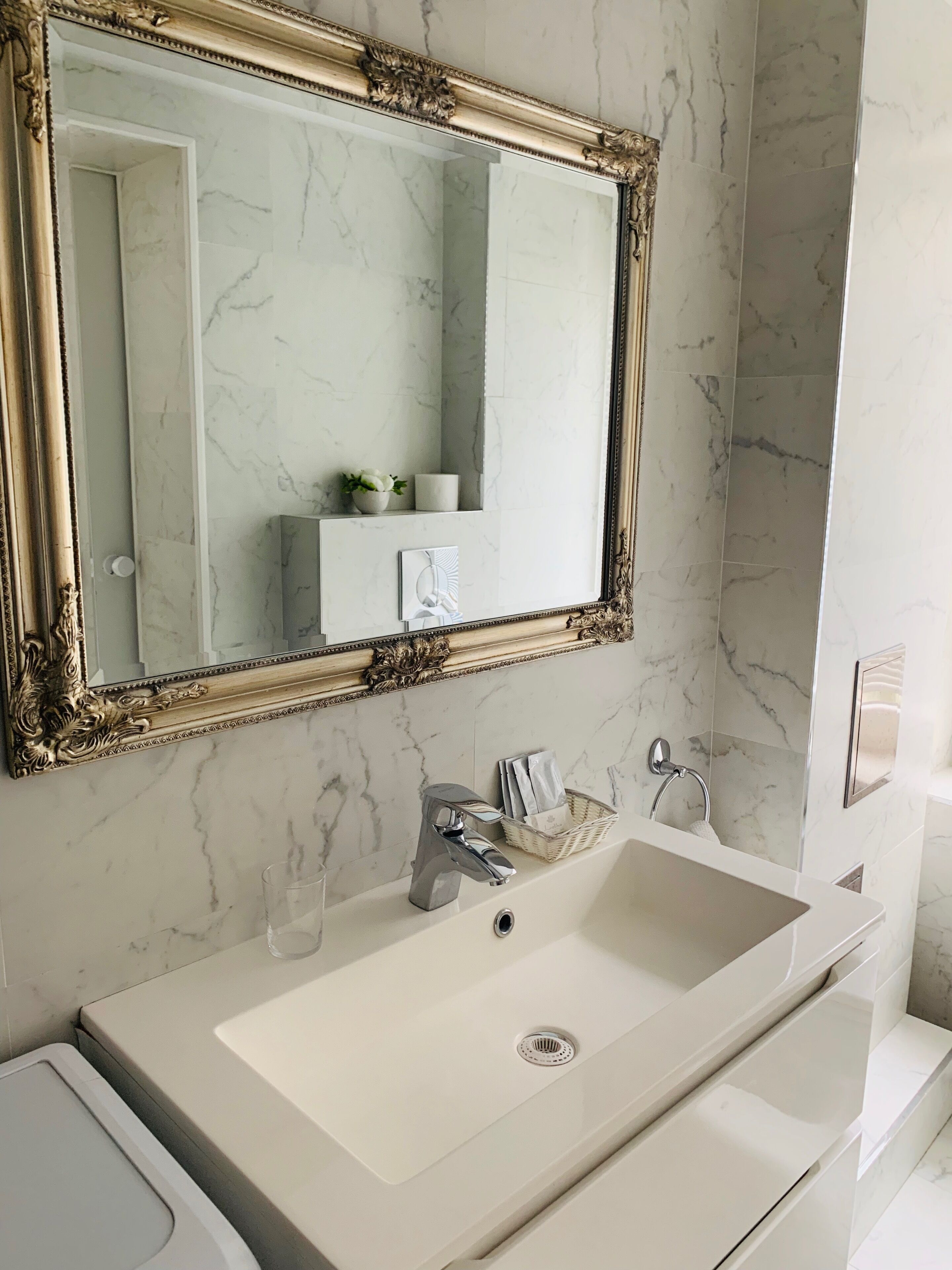A bathroom with a large mirror, marble walls, a white sink, and a towel rack.