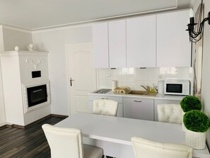 A modern kitchen with white cabinetry, a built-in microwave, and a central island with chairs. - Apartamenty Campari (Torun)