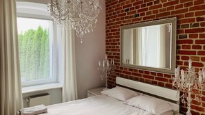 A bedroom with a brick wall, a large mirror, a chandelier, and a bed with white linens. - Apartamenty Campari (Torun)