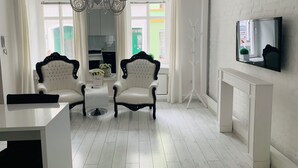 A modern living room with two upholstered chairs, a chandelier, a flat-screen TV mounted on the wall, and a view of the outside through large windows. - Apartamenty Campari (Torun)