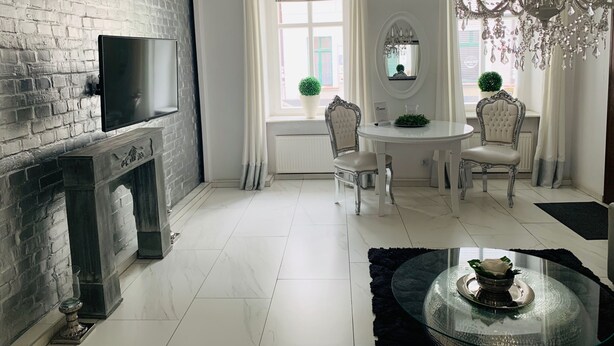 A modern living room with a fireplace, a round dining table, and two chairs. - Apartamenty Campari (Torun)