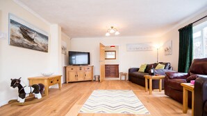 A cozy living room with a wooden floor, a television, a sofa, a rocking horse, and a chevron-patterned rug. - Spacious Family Bungalow with Garden & Annex (Laugharne)