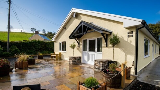 A house with a sloped roof, a stone fireplace, and a patio with potted plants. - Spacious Family Bungalow with Garden & Annex (Laugharne)