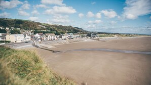 A coastal town with a sandy beach, houses, and a grassy hill in the background. - Spacious Family Bungalow with Garden & Annex (Laugharne)