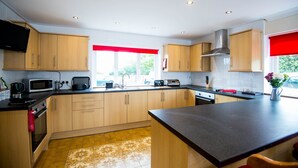 A modern kitchen with wooden cabinets, a central island, and built-in appliances. - Spacious Family Bungalow with Garden & Annex (Laugharne)