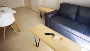 Un salon avec un canapé gris foncé, un fauteuil blanc et deux tables en bois.