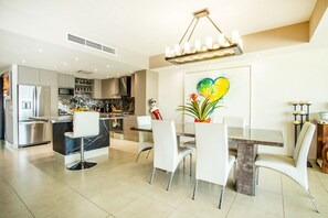 A modern kitchen with a central island, white chairs, and a dining table. - Spacious View Condo | Pools, Gym, Family Friendly (Puerto Vallarta)