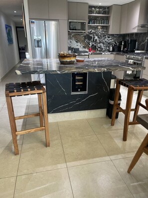 A modern kitchen with a marble island, stainless steel appliances, and wooden stools.