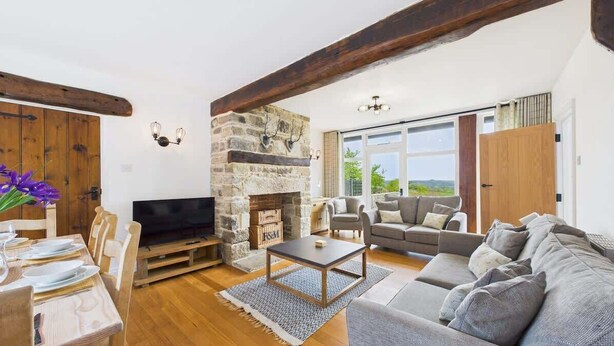 A living room with a stone fireplace, a sofa, a television, and a dining area with wooden furniture. - Tithe Barn, Little Upton Farm (Ashey)