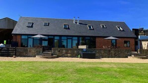 A modern building with a flat roof, multiple windows, and a stone wall. - Tithe Barn, Little Upton Farm (Ashey)