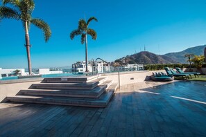 Ein Poolbereich auf dem Dach mit Stufen zum Pool, Liegestühlen und Palmen.
