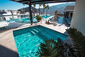 Une piscine à débordement située sur le toit, avec une eau d’un bleu cristallin, entourée de chaises longues et de parasols, et offrant une vue imprenable sur un paysage montagneux.