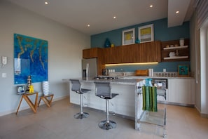 Una cocina moderna con una isla central, taburetes de bar, armarios de madera y un cuadro abstracto azul en la pared.