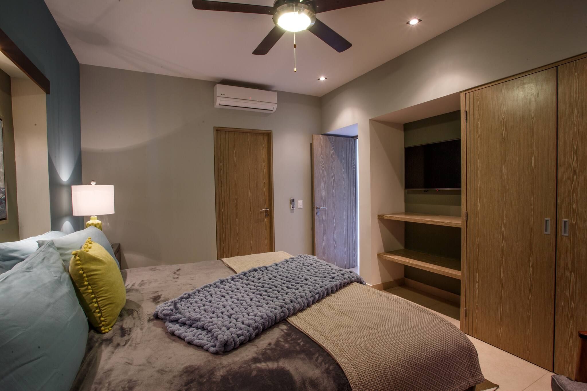 Quarto com cama, ventoinha no teto, aparelho de ar condicionado, guarda-roupa e abajur.