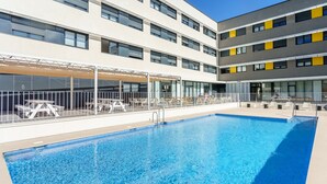 A swimming pool adjacent to a multi-story building with outdoor seating and a covered area. - Residencia Universitaria Resa Campus Málaga (Málaga)