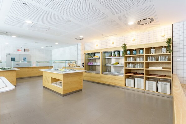 Un vestíbulo moderno y luminoso con una mesa de recepción, estanterías de madera con frascos y plantas, y suelo de baldosas.