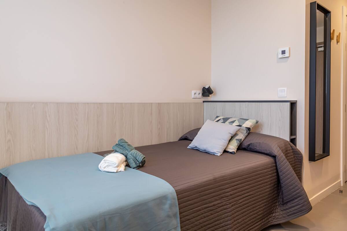 A neatly made bed with a brown bedspread and pillows, a blue blanket, and a folded towel on the side.