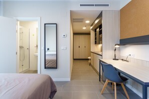 A modern hotel room with a bed, a desk, and a mirror. There is a shower area visible in the background. - Residencia Universitaria Resa Campus Málaga (Málaga)