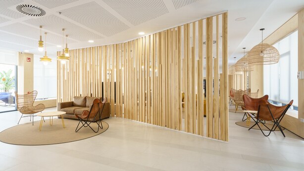 A modern interior with a curved wooden partition, a sofa, and two dining areas with chairs. - Residencia Universitaria Resa Campus Málaga (Málaga)