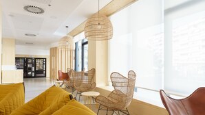 A modern interior with a yellow sofa, wicker chairs, and a vending machine area. - Residencia Universitaria Resa Campus Málaga (Málaga)