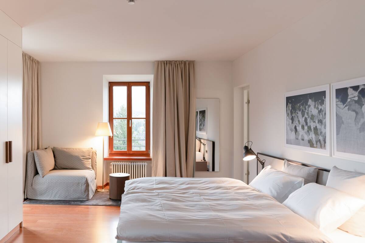 Une chambre moderne avec un grand lit, un canapé, une fenêtre avec des rideaux et des œuvres d’art accrochées au mur.