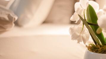 Une orchidée blanche dans un vase blanc, posée sur un lit, avec un arrière-plan flou.