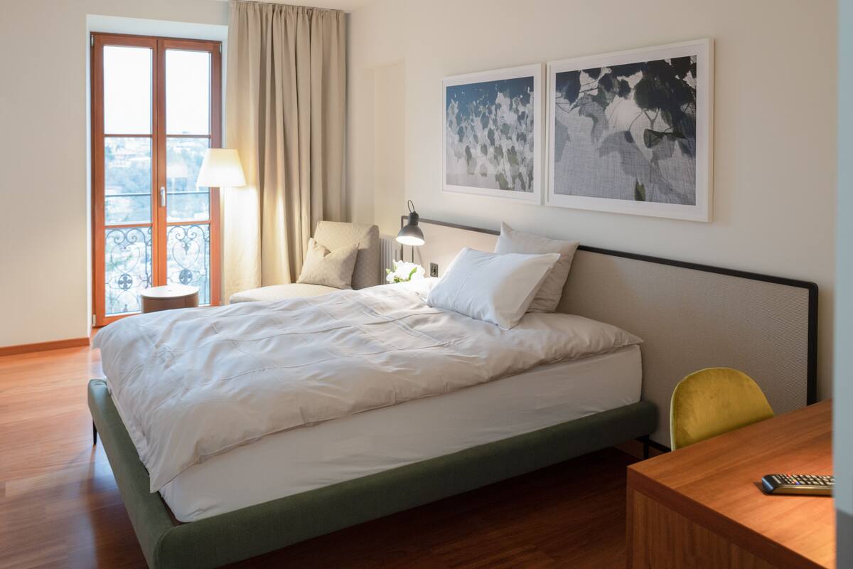Une chambre d’hôtel avec un lit, une chaise, une table et une fenêtre avec des rideaux.