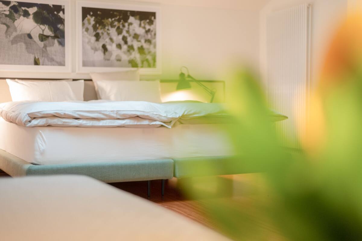 Une chambre à coucher avec un lit, une table de chevet, une lampe et une œuvre d’art accrochée au mur.