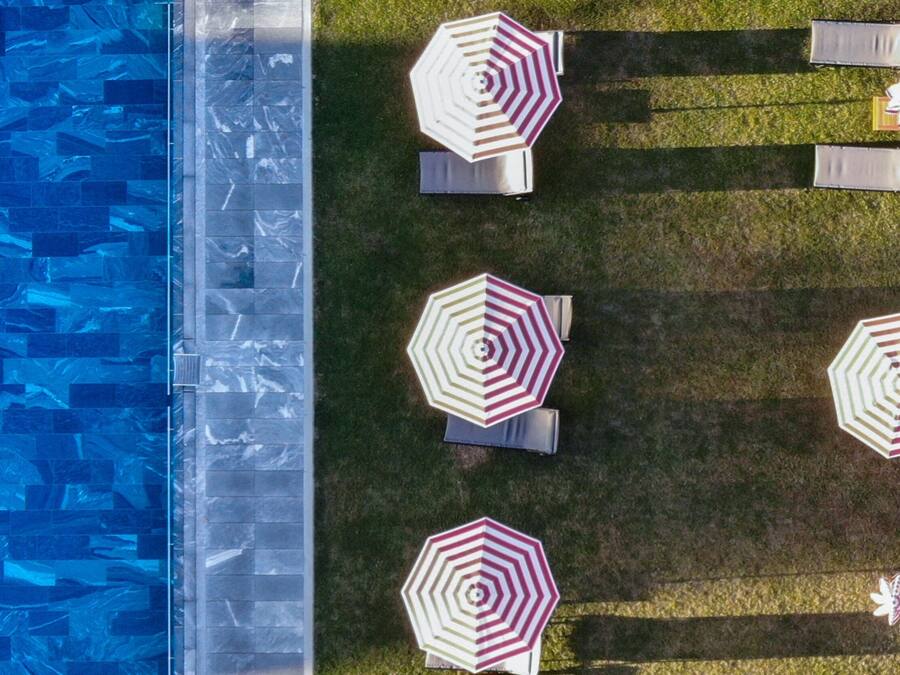 Vista aérea de una zona de piscina con múltiples sombrillas hexagonales y sillones de descanso dispuestos sobre un césped.