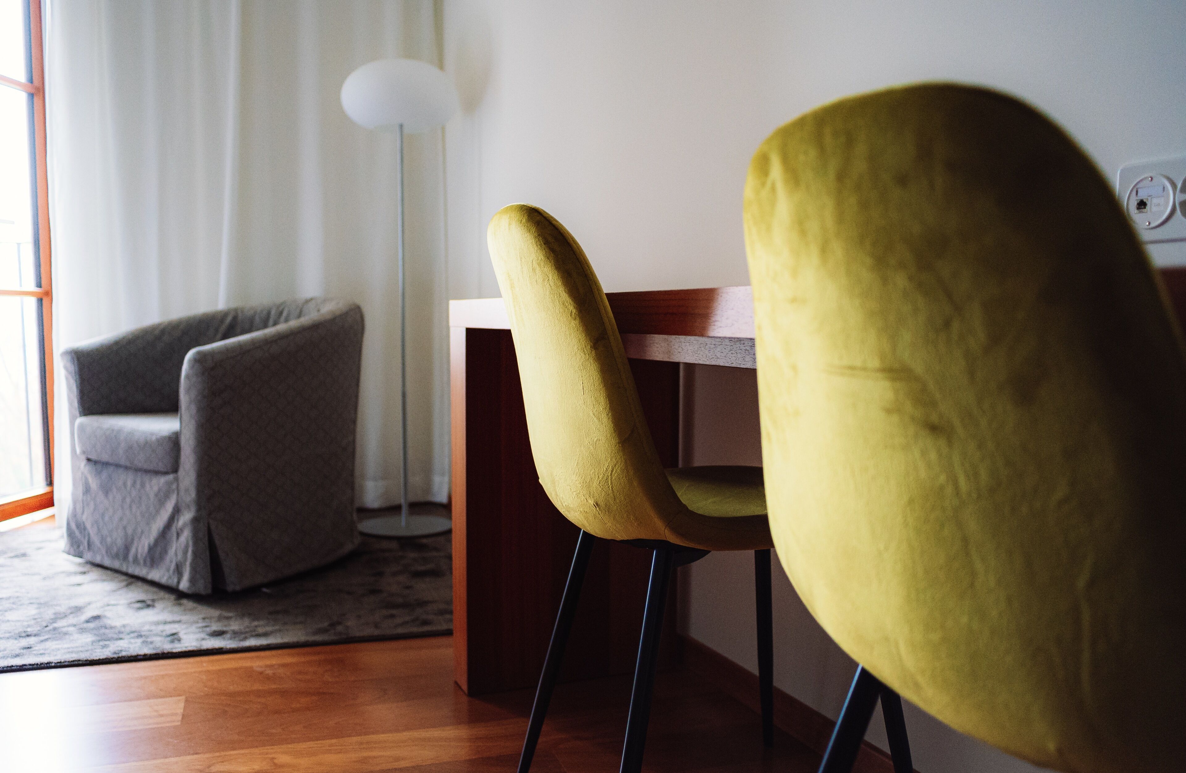 Ein Zimmer mit Holzboden, einem grauen Sessel, einem gelben Stuhl und einer weißen Lampe.