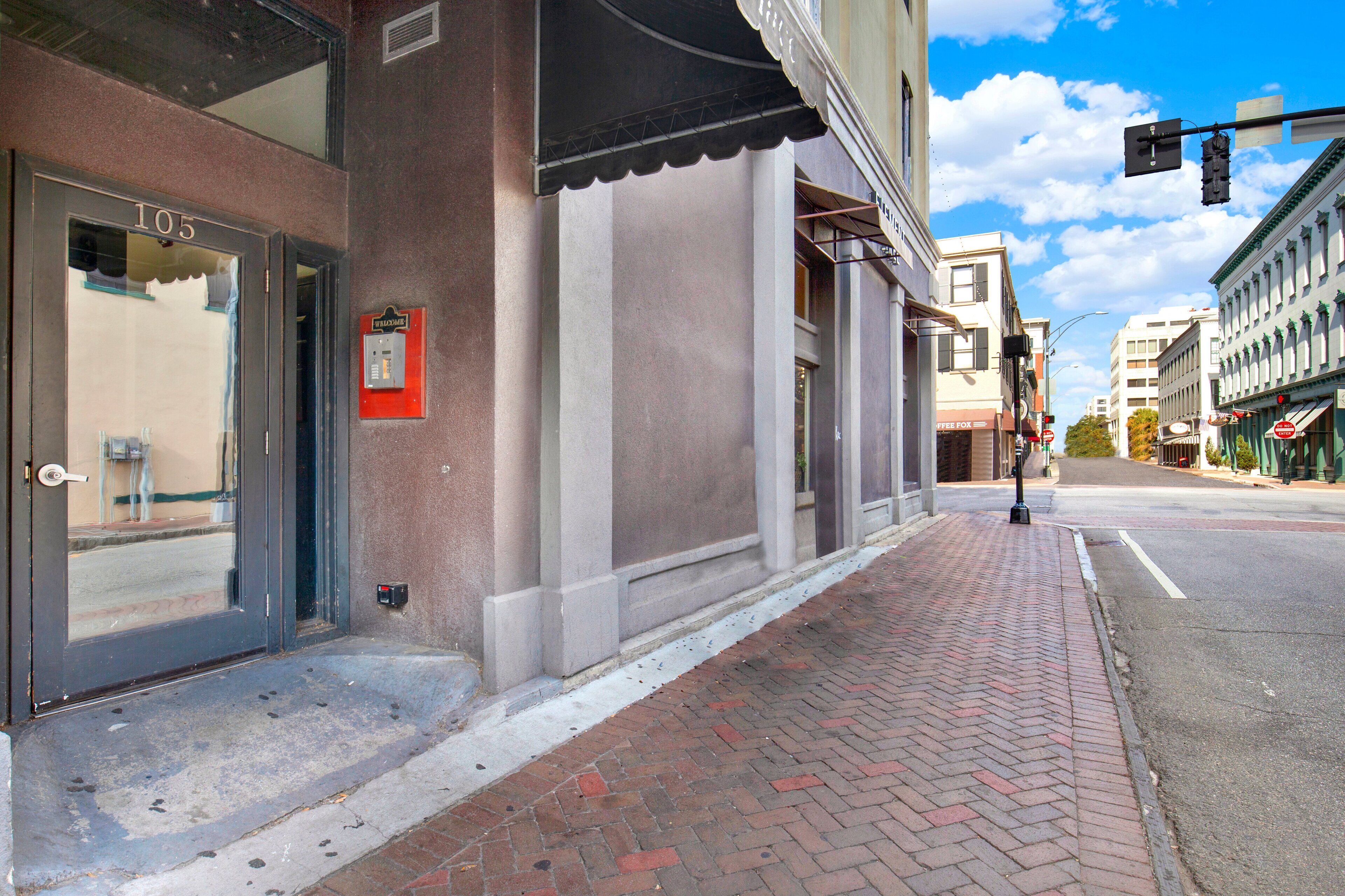 A building with a storefront, a fire alarm, and a brick sidewalk.