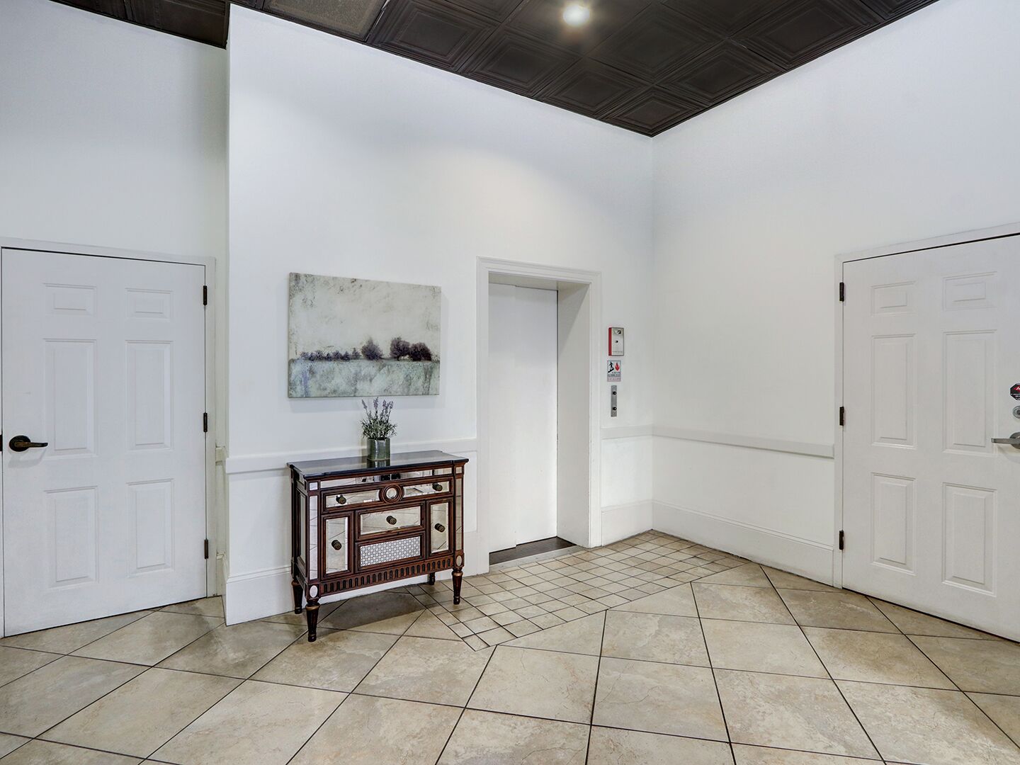 A hallway with white walls, a tiled floor, and a wooden console table with a vase.