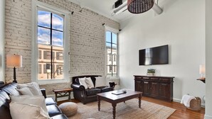 A living room with a leather sofa, a wooden coffee table, and a large window with a view of buildings. - Broughton Retreat in the Heart of Downtown! (Savannah)