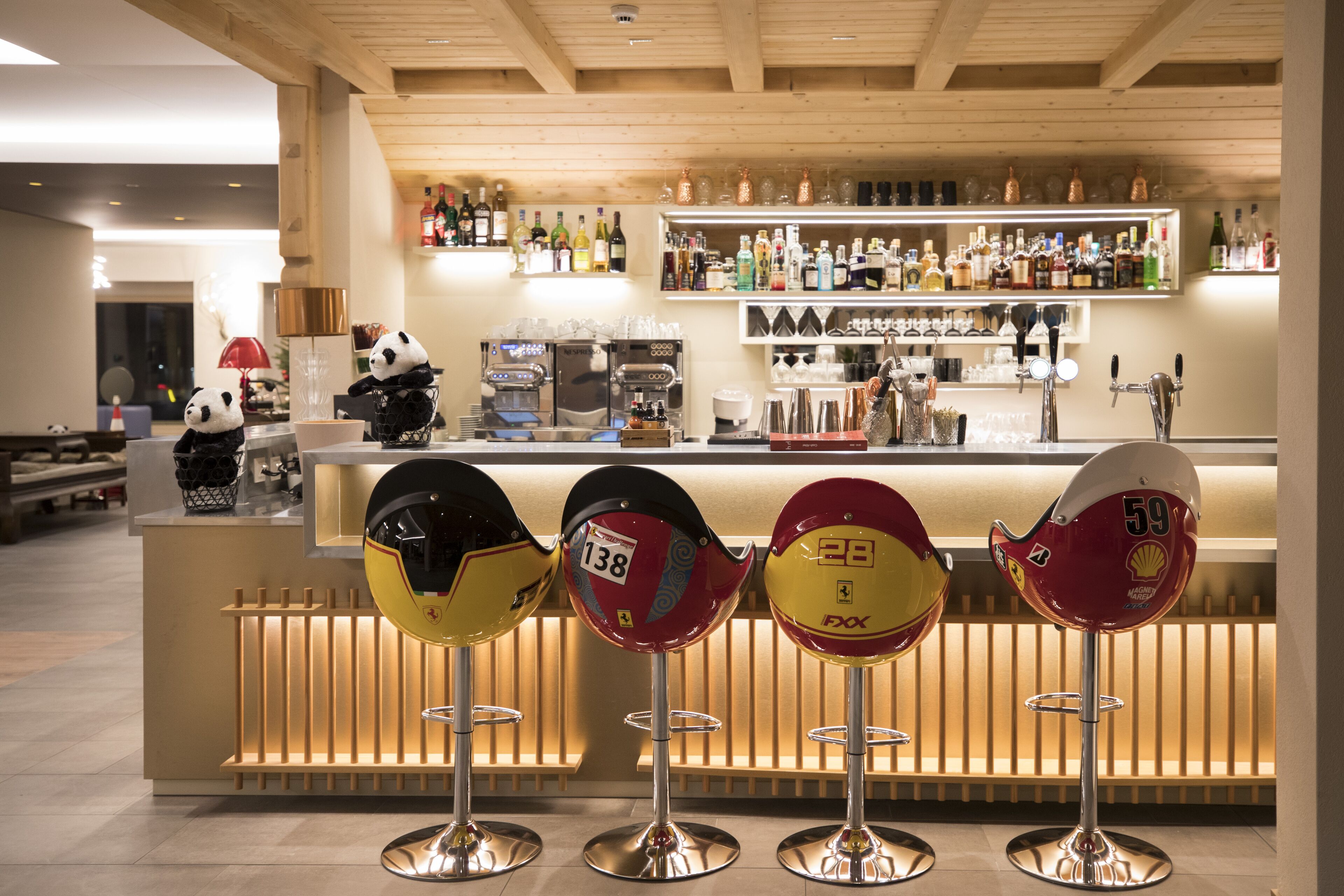 A bar area with a counter, shelves of bottles, and four stools with racing numbers.