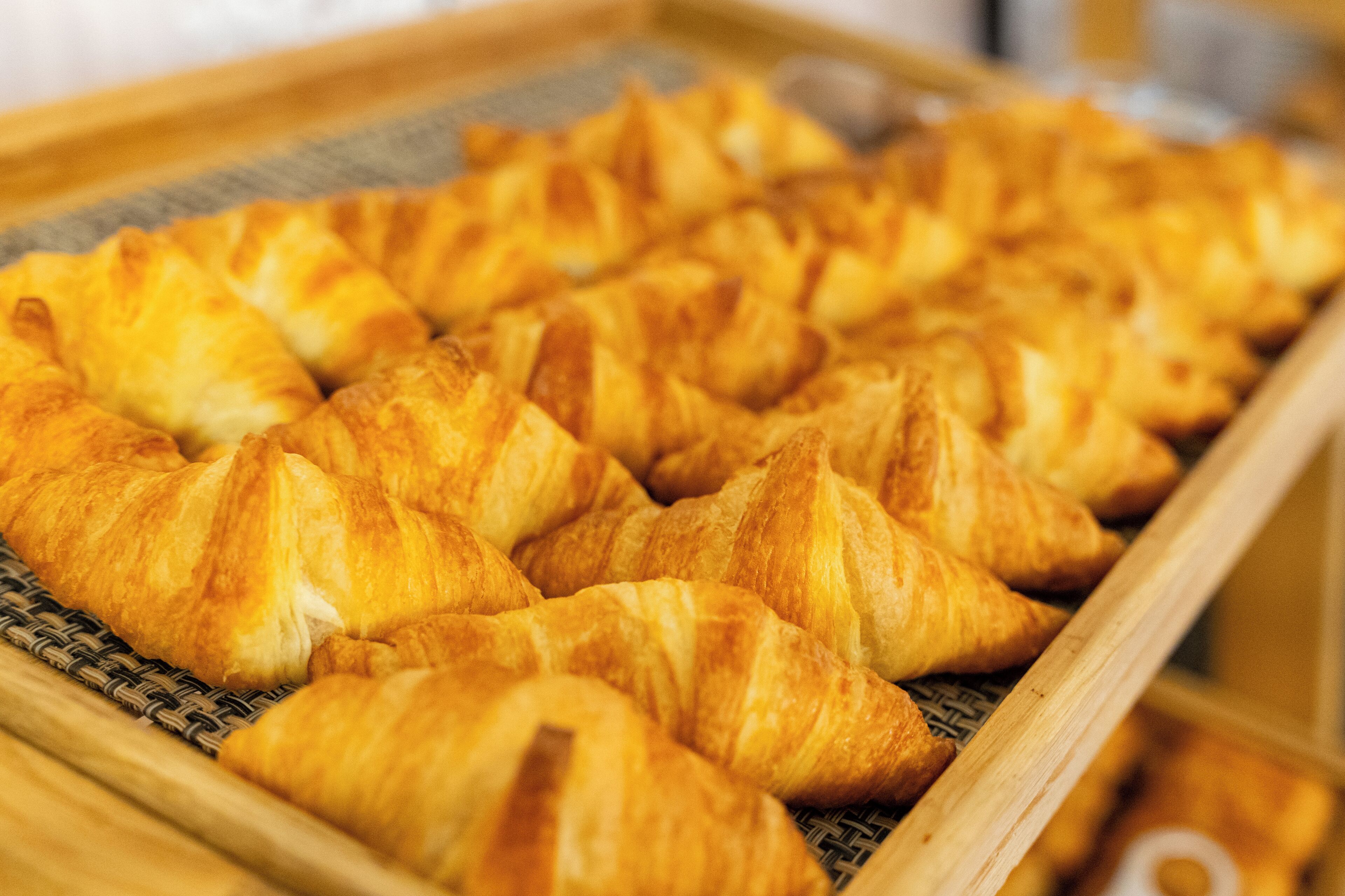 A tray of golden-brown croissants arranged neatly on a woven mat.