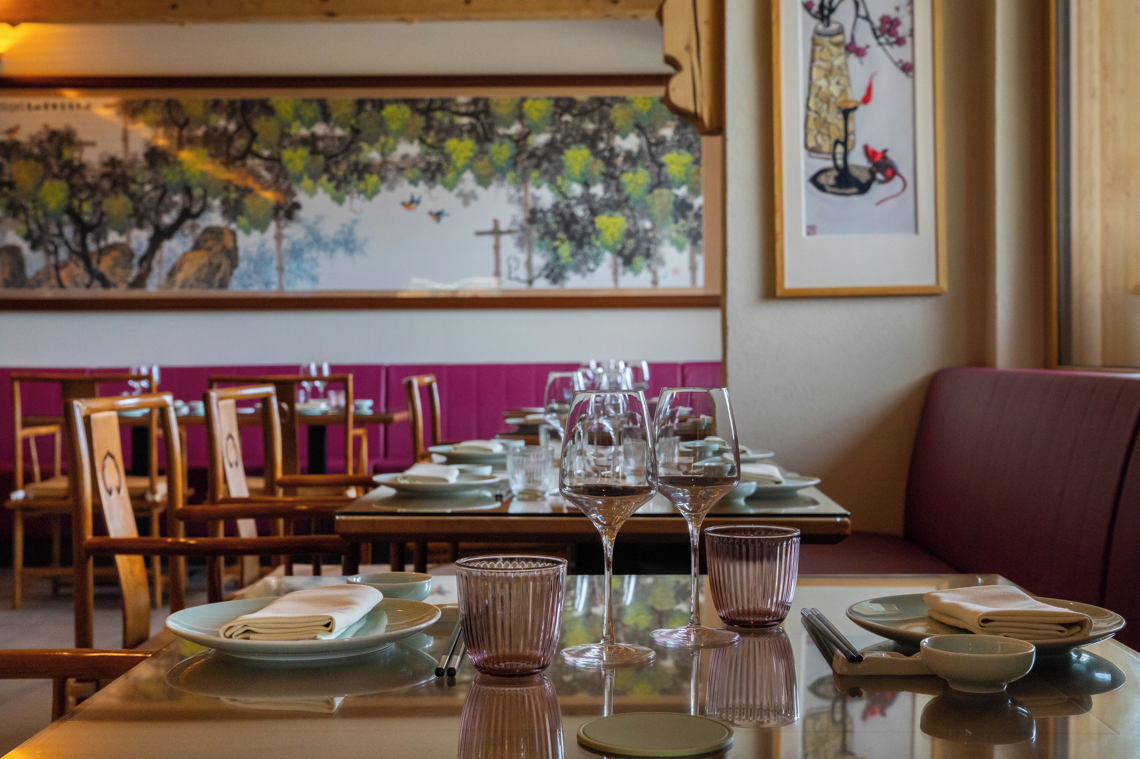 A dining area with tables set for a meal, chairs, and a painting on the wall.