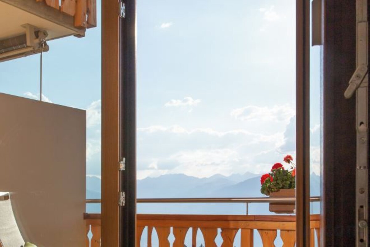 A balcony with a view of mountains and a wooden railing.
